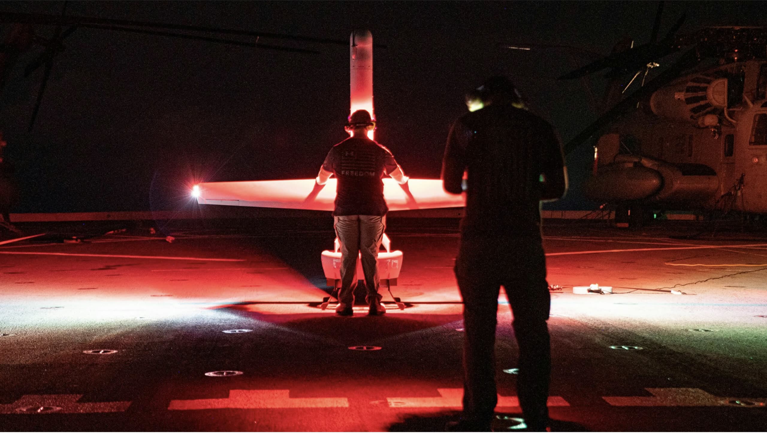 UAV lit at night on a ship deck during launch ops